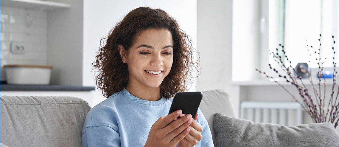 Uma menina negra com cabelos cacheados olha o celular em sua mão e sorri.